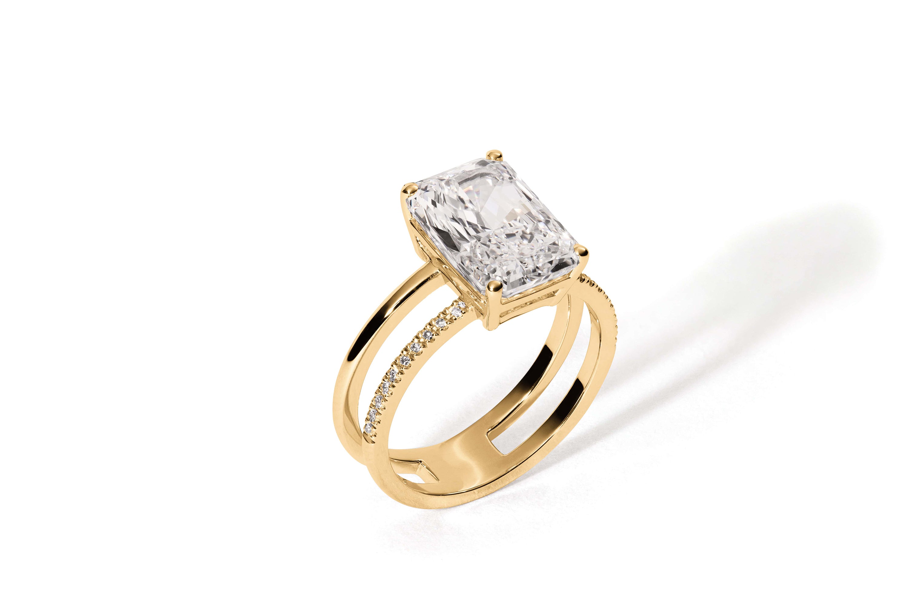 Der Ring APHRODITE GELBGOLD von Atelier Sofia ist mit einem im Radiantschliff gefertigten, im Labor gezüchteten Diamanten aus 18 Karat Gelbgold versehen. Der große Diamant wird von vier Zinken gehalten und krönt ein doppellagiges Band, das mit kleinen Diamanten geschmückt ist, die auf einem schlichten weißen Hintergrund angeordnet sind und einen zarten Schatten werfen.