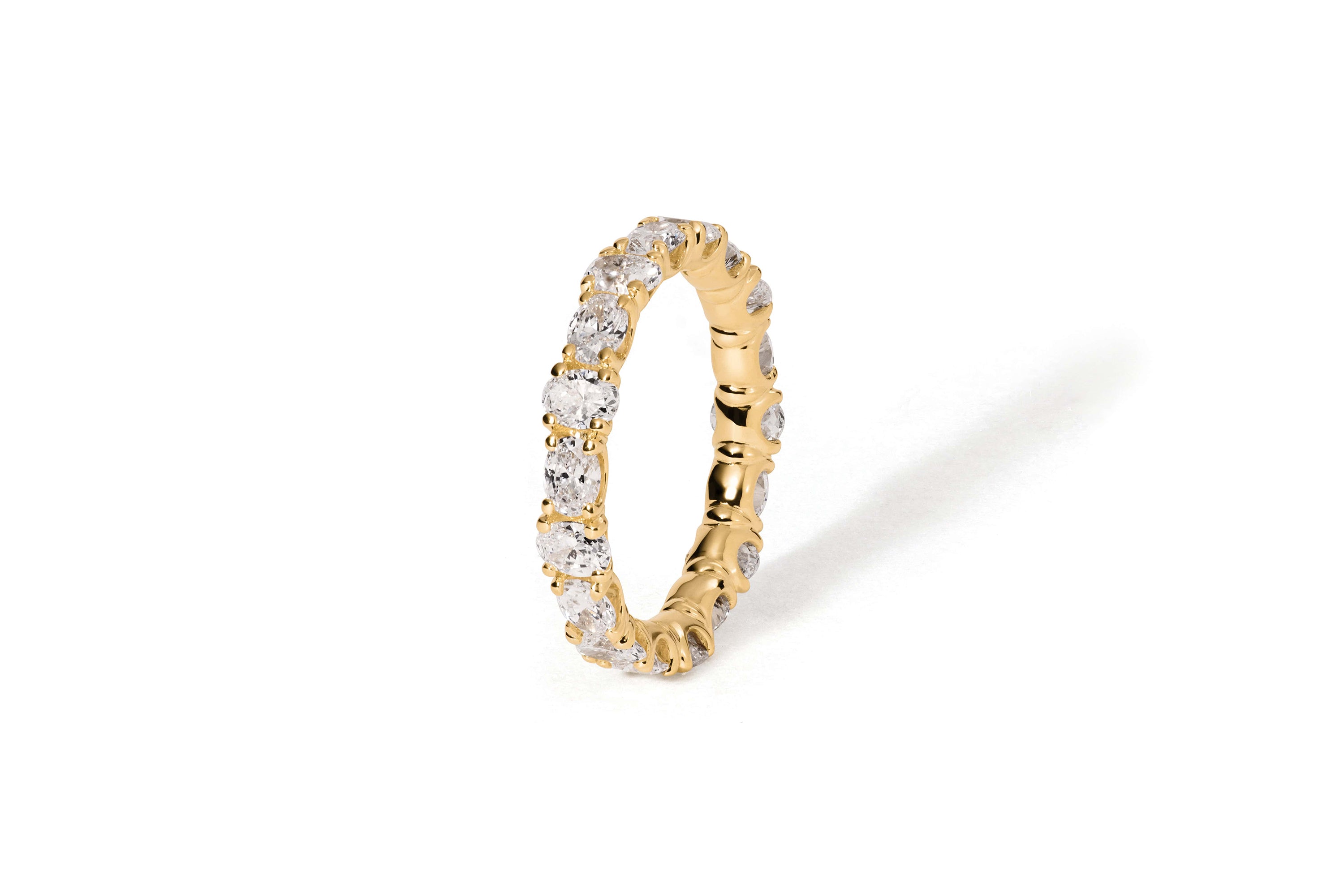 Der Eternity-Ring KALLIOPI GELBGOLD von Atelier Sofia ist mit funkelnden, im Labor gezüchteten Diamanten in 18 Karat Gelbgold ausgestattet, die den Ring vollständig umschließen. Aufrecht auf einem schlichten weißen Hintergrund platziert, wirft er einen schwachen Schatten nach rechts.